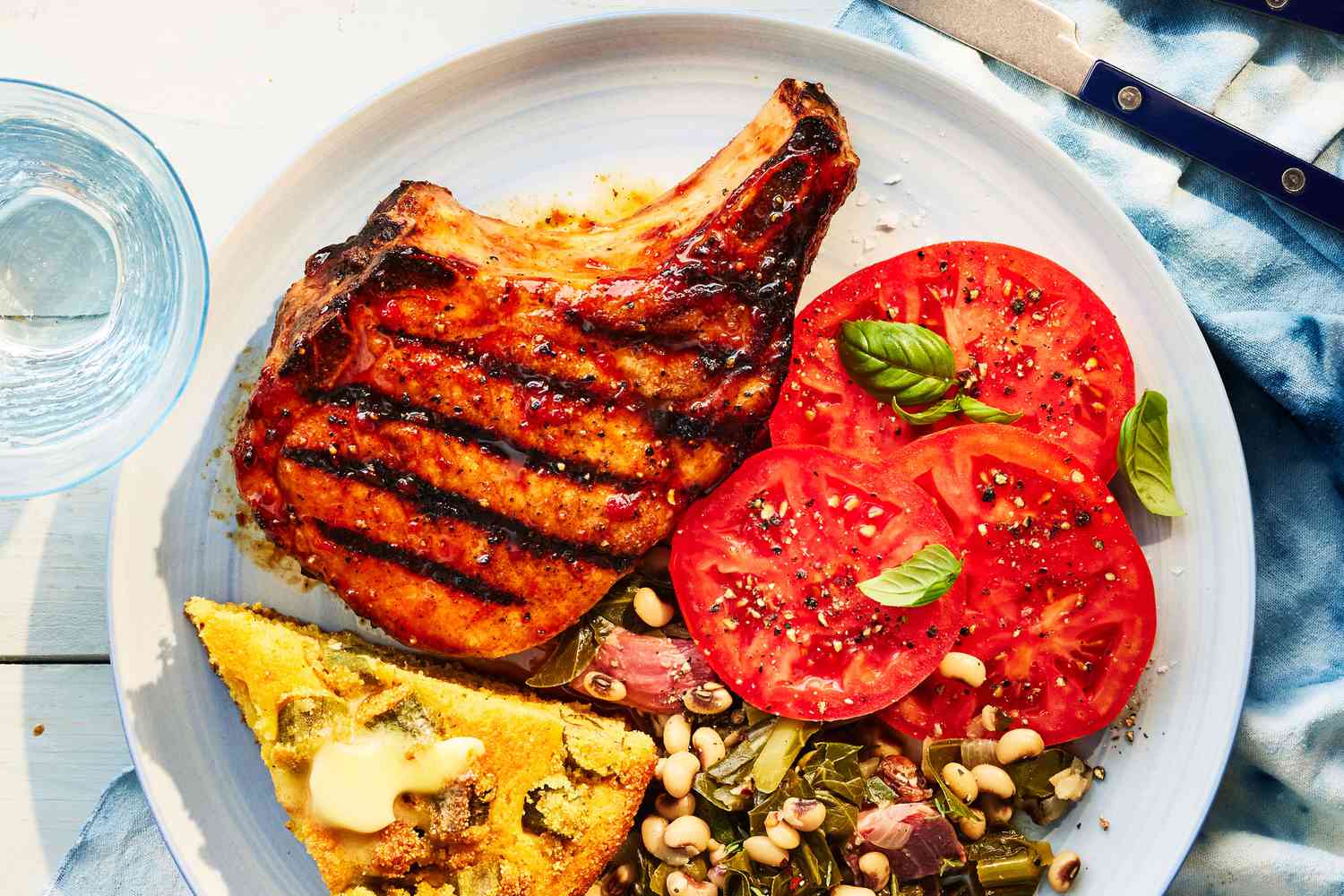 Southern Living Pepper Jelly-Glazed Pork Chops on a plate with tomatoes, cornbread, and lady peas and greens