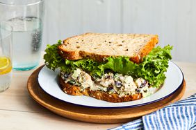 A cranberry chicken salad sandwich on a white plate with cups of water