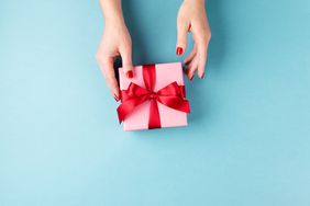 Female hands holding gift box on blue background.