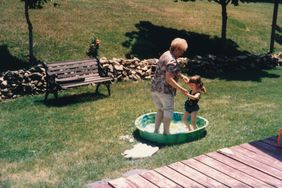 Active senior citizen grandmother playing with granddaughter outside in baby pool. Conceptual image for togetherness, family bonding and grandparents love.