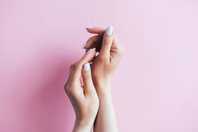 Female hands with white manicure on a pink background.