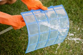 Person cleaning air filter with orange gloves on and hose