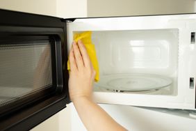 a woman's hand washes a microwave with a rag