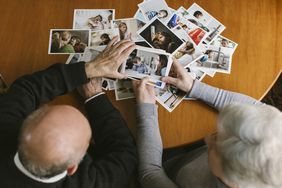 An overhead photo of a senior couple looking at printed photos on a wooden table 