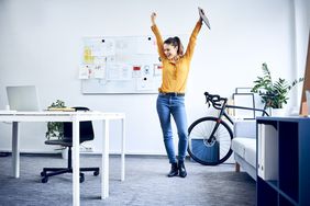 Happy young businesswoman cheering in office