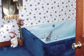 bright blue carpet runs up along the sides of the tub and outdated wallpaper with small flowers off-sets this dated master bathroom